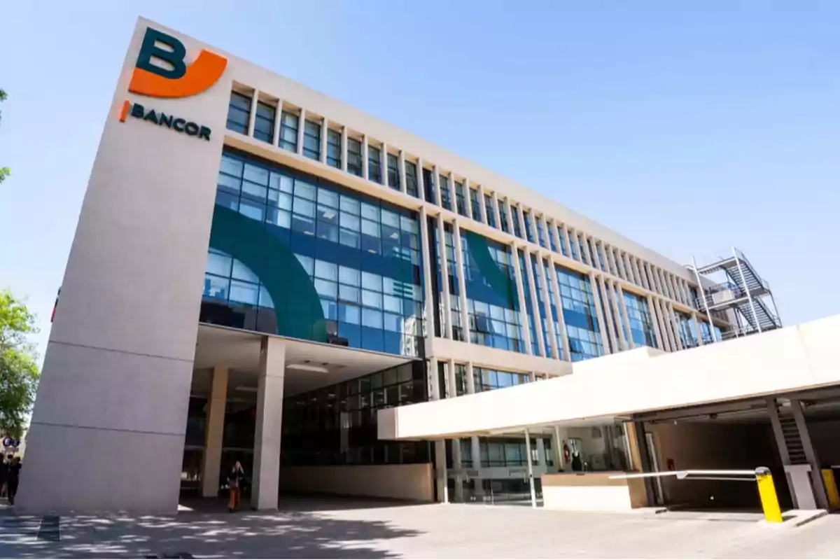 Modern office building with a glass facade and the Bancor logo in the upper left corner under a clear sky