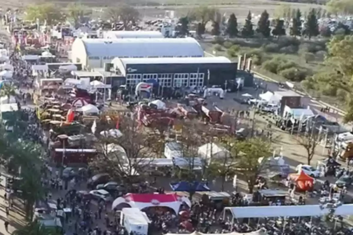 Aerial view of an outdoor fair with numerous stalls, tents, agricultural machinery, and a large number of people walking around the area. Aerial view of an outdoor fair with numerous stalls, tents, agricultural machinery, and a large number of people walking around the area.
