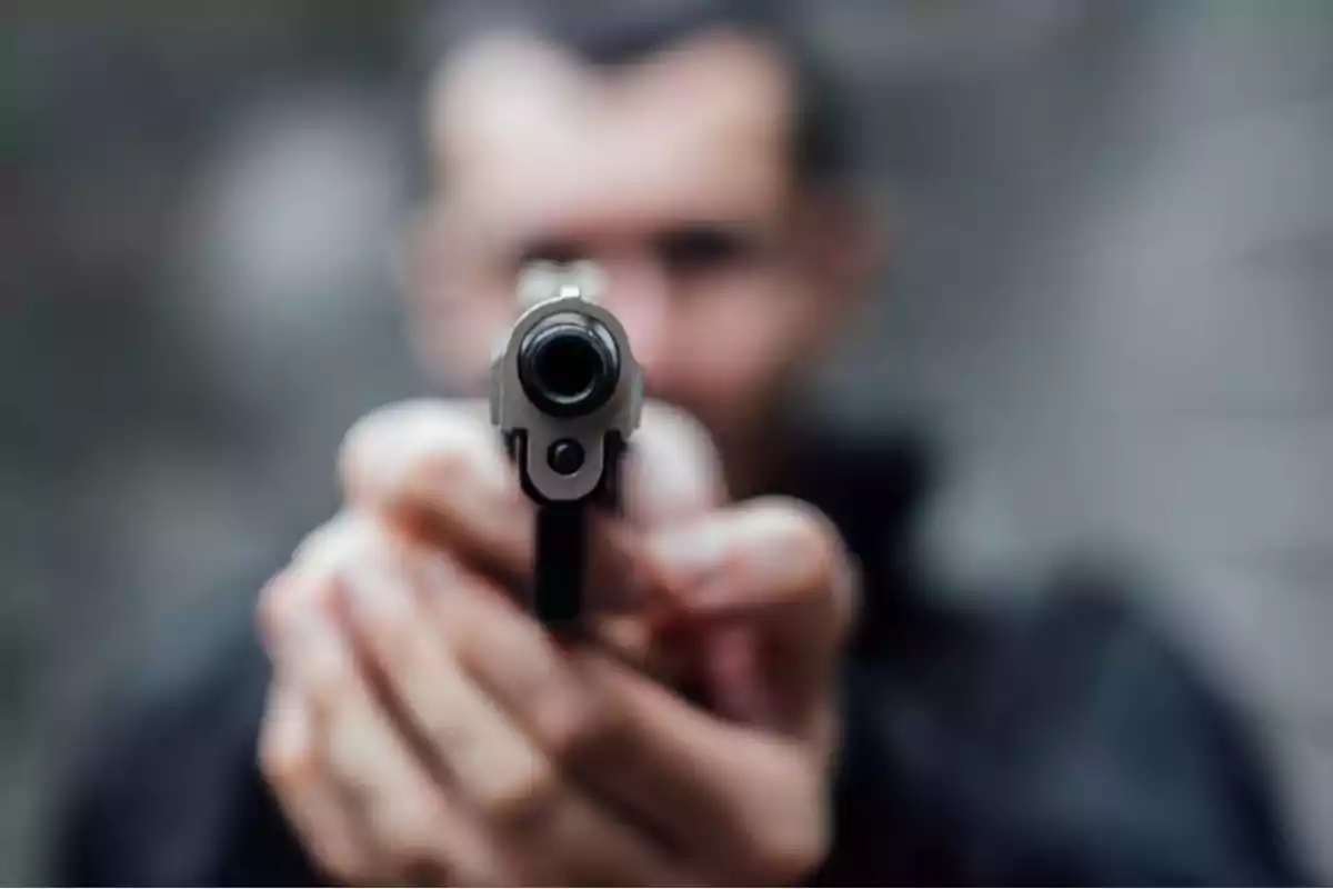 Persona sosteniendo una pistola apuntando hacia la cámara con el fondo desenfocado