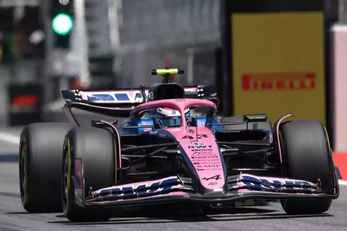 A pink and blue Formula 1 single-seater is driving on a track during a race. A pink and blue Formula 1 single-seater is driving on a track during a race.