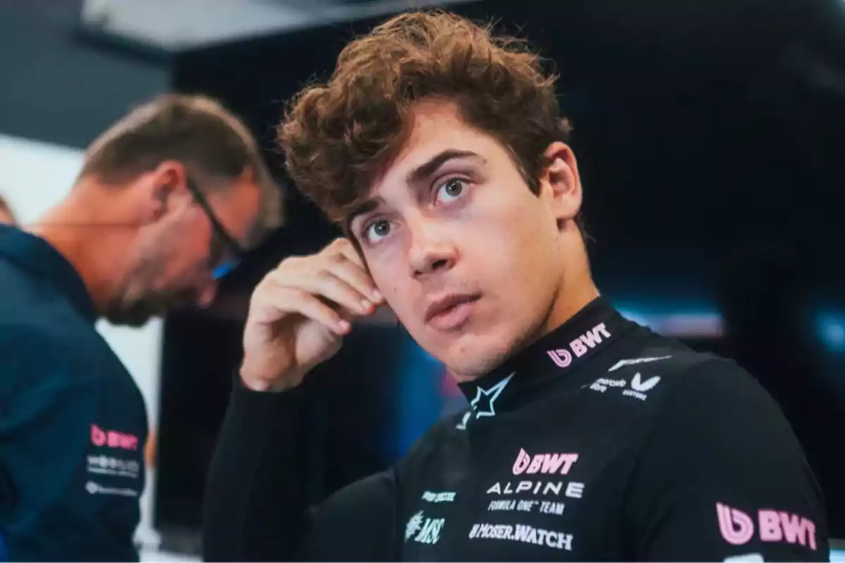 Young motorsport driver in a black Alpine team uniform looking at the camera while adjusting his earpiece