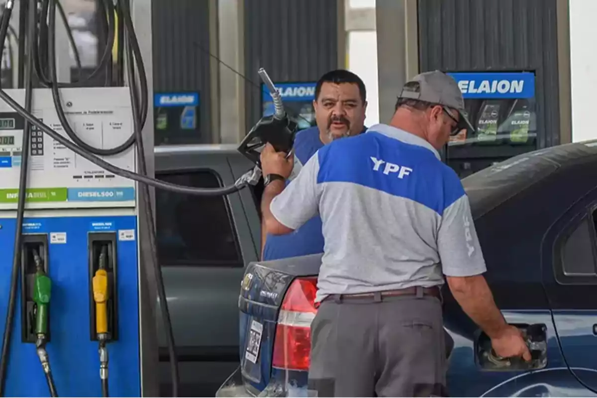 Un empleado de estación de servicio YPF carga combustible en un auto mientras otro hombre observa