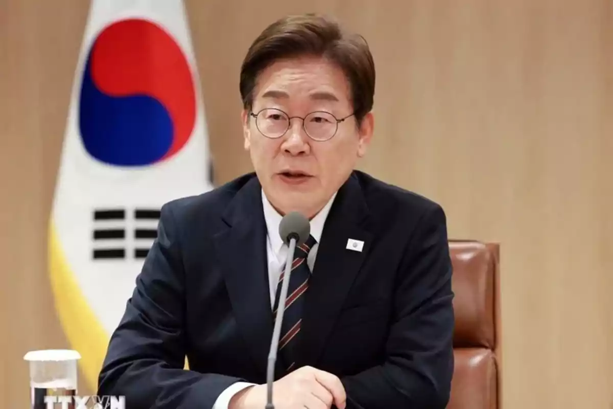 Man with glasses and a dark suit speaking in front of a microphone with a South Korean flag in the background Man with glasses and a dark suit speaking in front of a microphone with a South Korean flag in the background