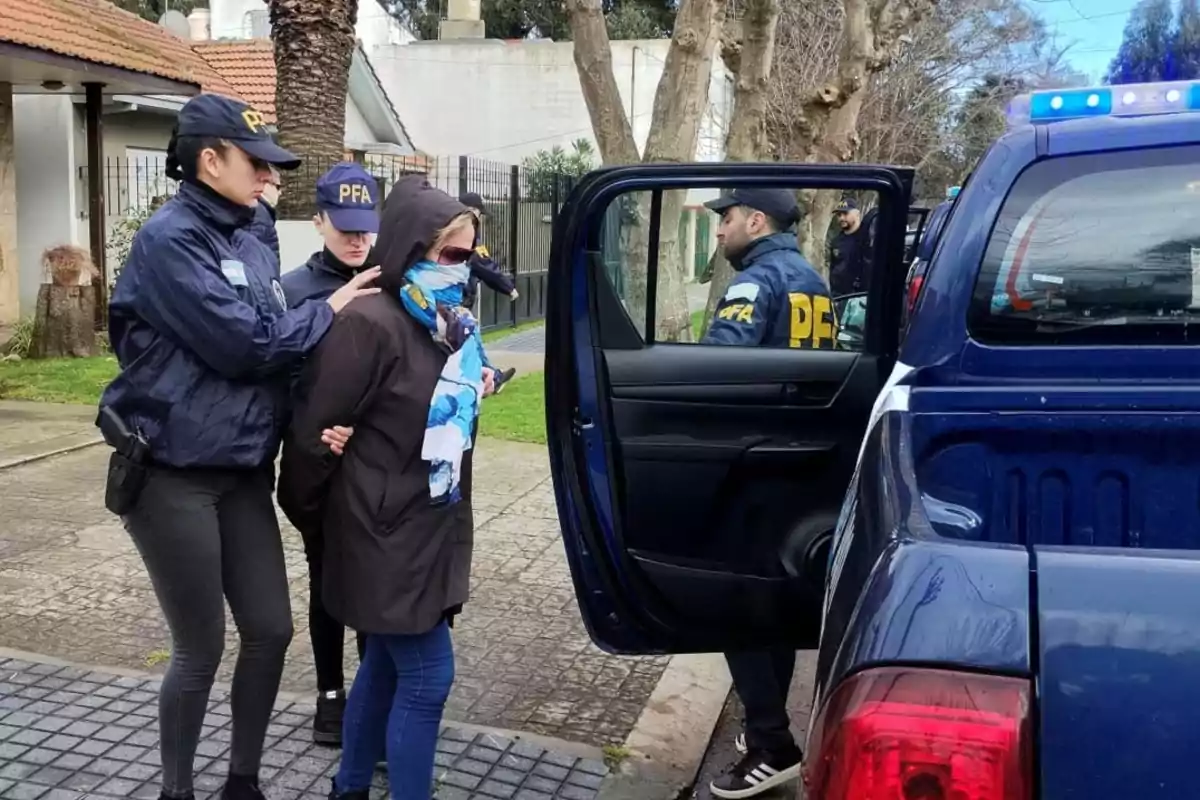 Policías escoltan a una mujer esposada hacia una camioneta policial en la vía pública