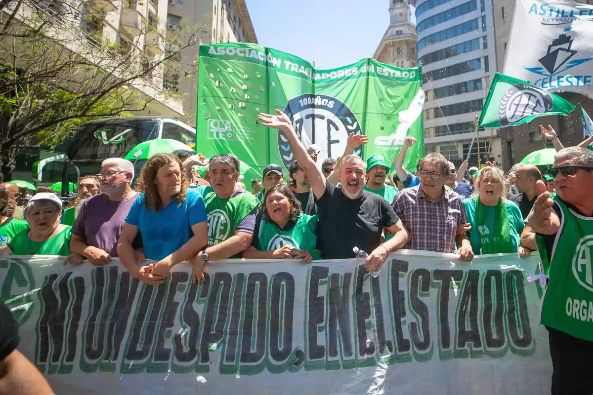Manifestación de trabajadores con pancartas y banderas verdes en una calle de la ciudad exigiendo que no haya despidos en el sector estatal Manifestación de trabajadores con pancartas y banderas verdes en una calle de la ciudad exigiendo que no haya despidos en el sector estatal
