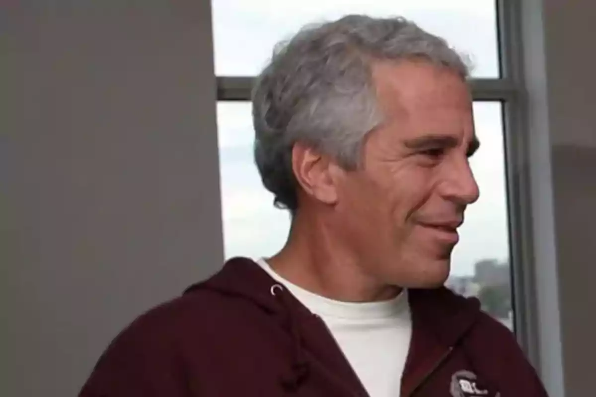 Gray-haired man with short hair wearing a burgundy sweatjersey and a white t-jersey in profile in a room with a window in the background