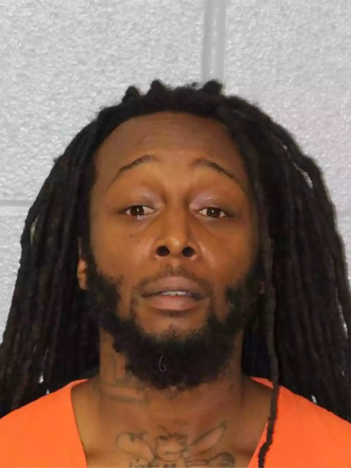 Man with dreadlocks and a beard, wearing an orange uniform, posing in front of a gray wall Man with dreadlocks and a beard, wearing an orange uniform, posing in front of a gray wall