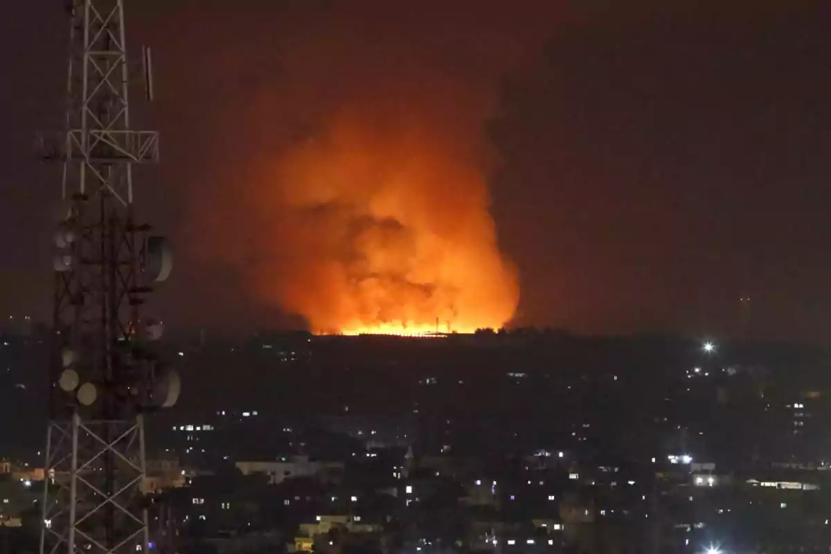 Incendio de gran magnitud en el horizonte de una ciudad durante la noche con una torre de telecomunicaciones en primer plano Incendio de gran magnitud en el horizonte de una ciudad durante la noche con una torre de telecomunicaciones en primer plano
