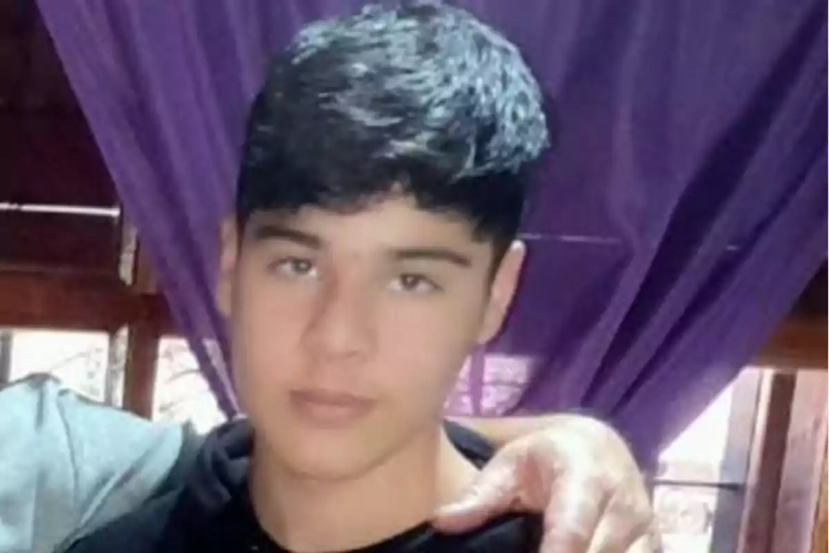 Young man with short dark hair posing in front of a purple curtain