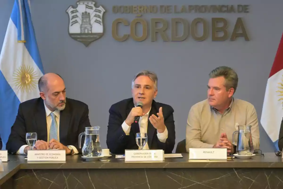 Tres hombres sentados en una mesa durante una conferencia de prensa en un salón oficial del gobierno de la provincia de Córdoba con banderas de Argentina y carteles institucionales de fondo