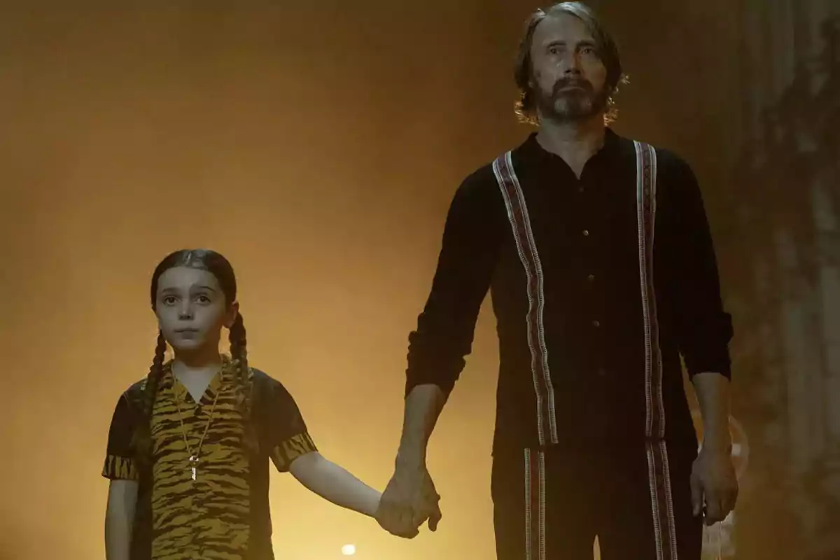 A man and a girl with braids hold hands and look straight ahead with serious expressions, illuminated by a warm light in the background. A man and a girl with braids hold hands and look straight ahead with serious expressions, illuminated by a warm light in the background.