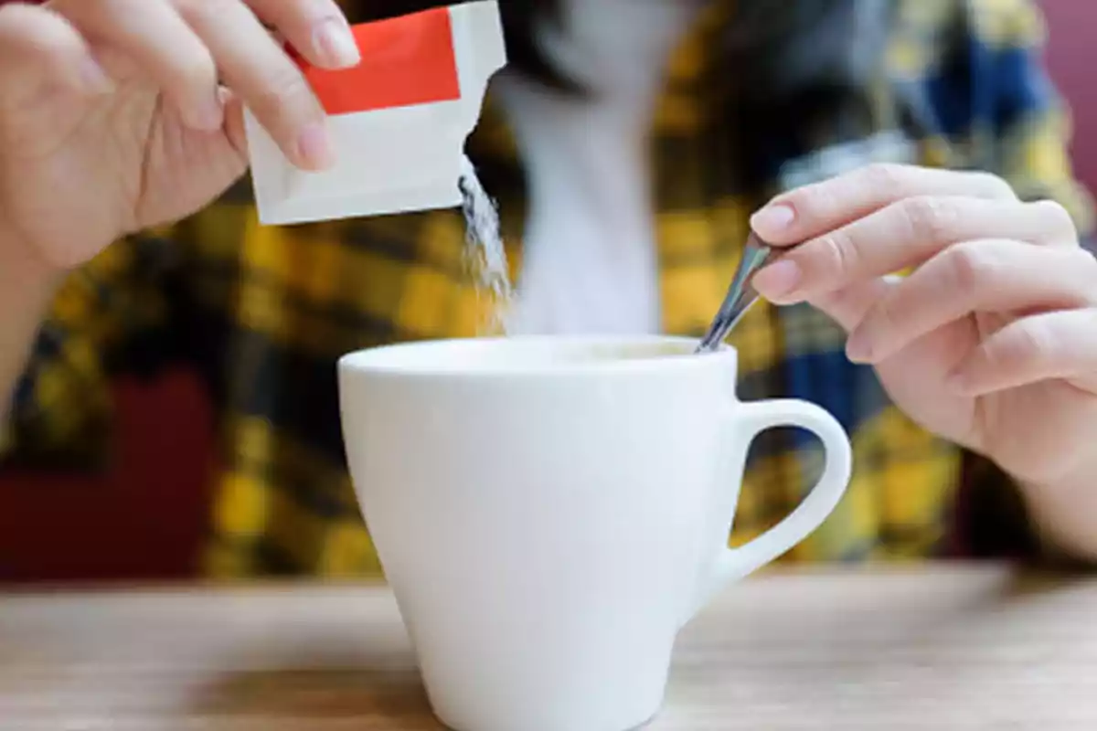 Person pouring sugar into a cup of coffee while holding a spoon Person pouring sugar into a cup of coffee while holding a spoon
