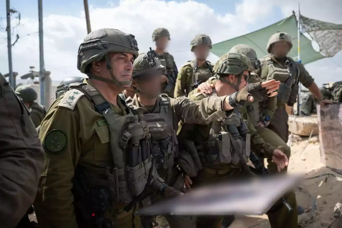 Un grupo de soldados con uniforme militar y equipo táctico se encuentra reunido al aire libre mientras uno de ellos señala hacia el horizonte Un grupo de soldados con uniforme militar y equipo táctico se encuentra reunido al aire libre mientras uno de ellos señala hacia el horizonte
