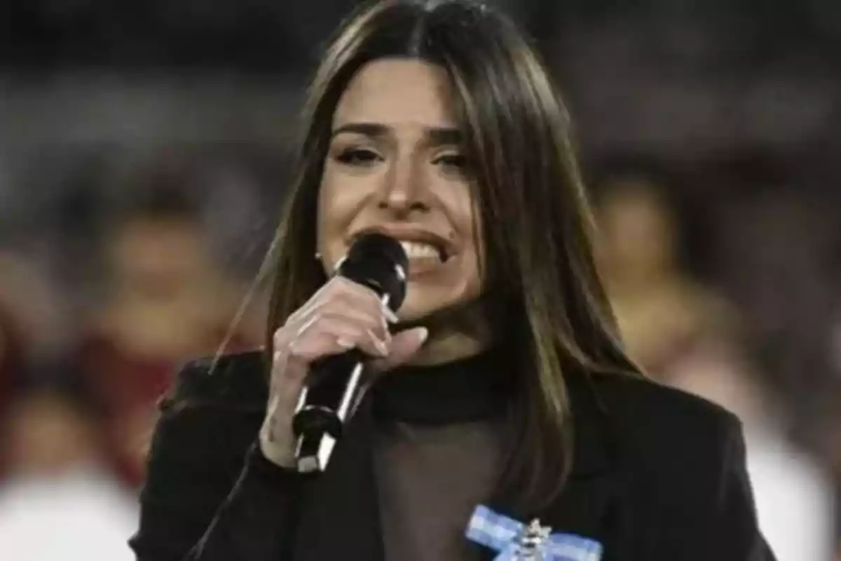Woman singing with a microphone in her hand and a light blue and white ribbon on her lapel