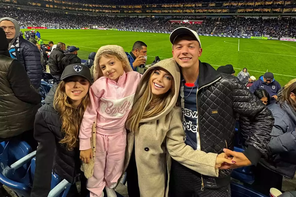 A smiling family posing in the stands of a packed soccer stadium at night, all bundled up and enjoying the sports atmosphere. A smiling family posing in the stands of a packed soccer stadium at night, all bundled up and enjoying the sports atmosphere.