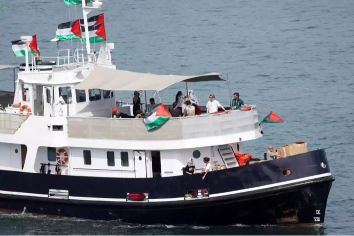 Un barco navega en el mar con varias personas a bordo y banderas palestinas ondeando en diferentes partes de la embarcación Un barco navega en el mar con varias personas a bordo y banderas palestinas ondeando en diferentes partes de la embarcación