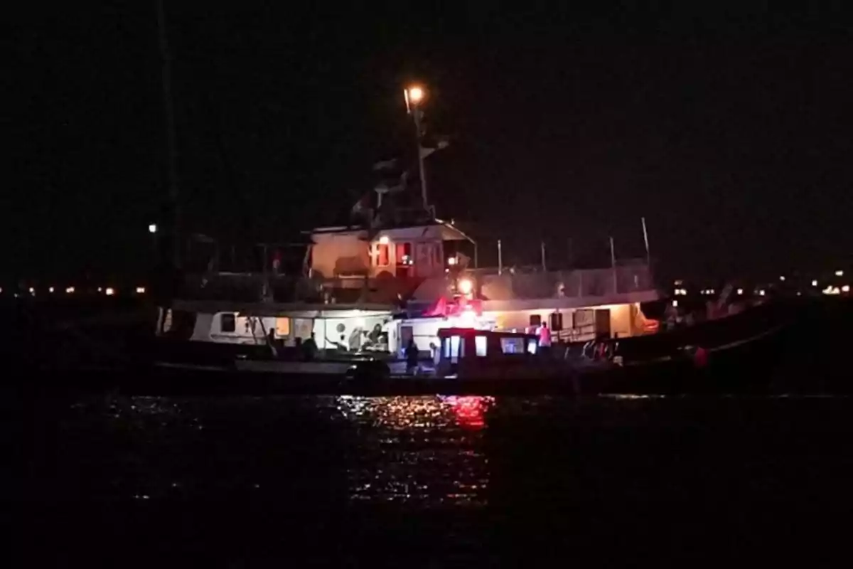 Un barco iluminado por luces rojas y blancas está en el mar durante la noche