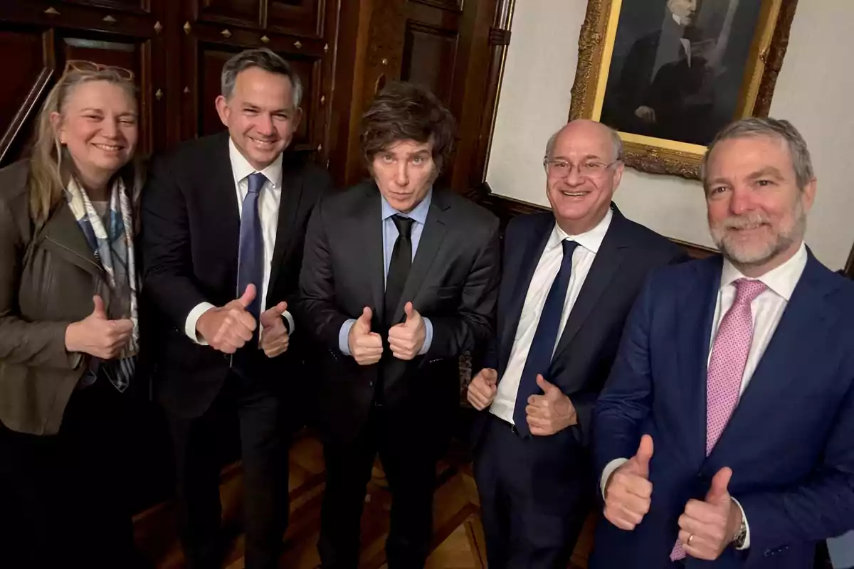 Cinco personas vestidas de manera formal posan sonriendo y levantando los pulgares en señal de aprobación dentro de una sala elegante con un retrato en la pared. Cinco personas vestidas de manera formal posan sonriendo y levantando los pulgares en señal de aprobación dentro de una sala elegante con un retrato en la pared.