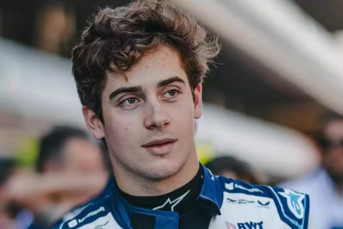 Young race car driver in a blue and white uniform looking to the side in an outdoor setting