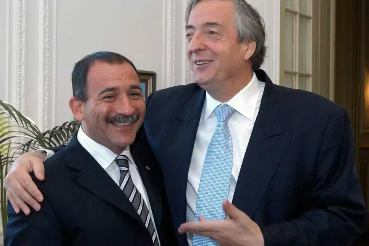Two men in suits smile and pose together in a formal setting.