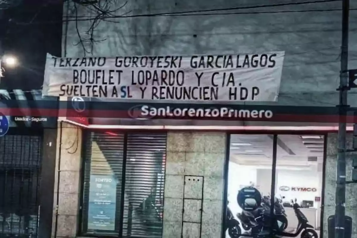 Pancarta colgada en la fachada de un edificio con un mensaje dirigido a varias personas pidiendo que suelten a San Lorenzo y renuncien, con un tono de protesta fuerte Pancarta colgada en la fachada de un edificio con un mensaje dirigido a varias personas pidiendo que suelten a San Lorenzo y renuncien, con un tono de protesta fuerte