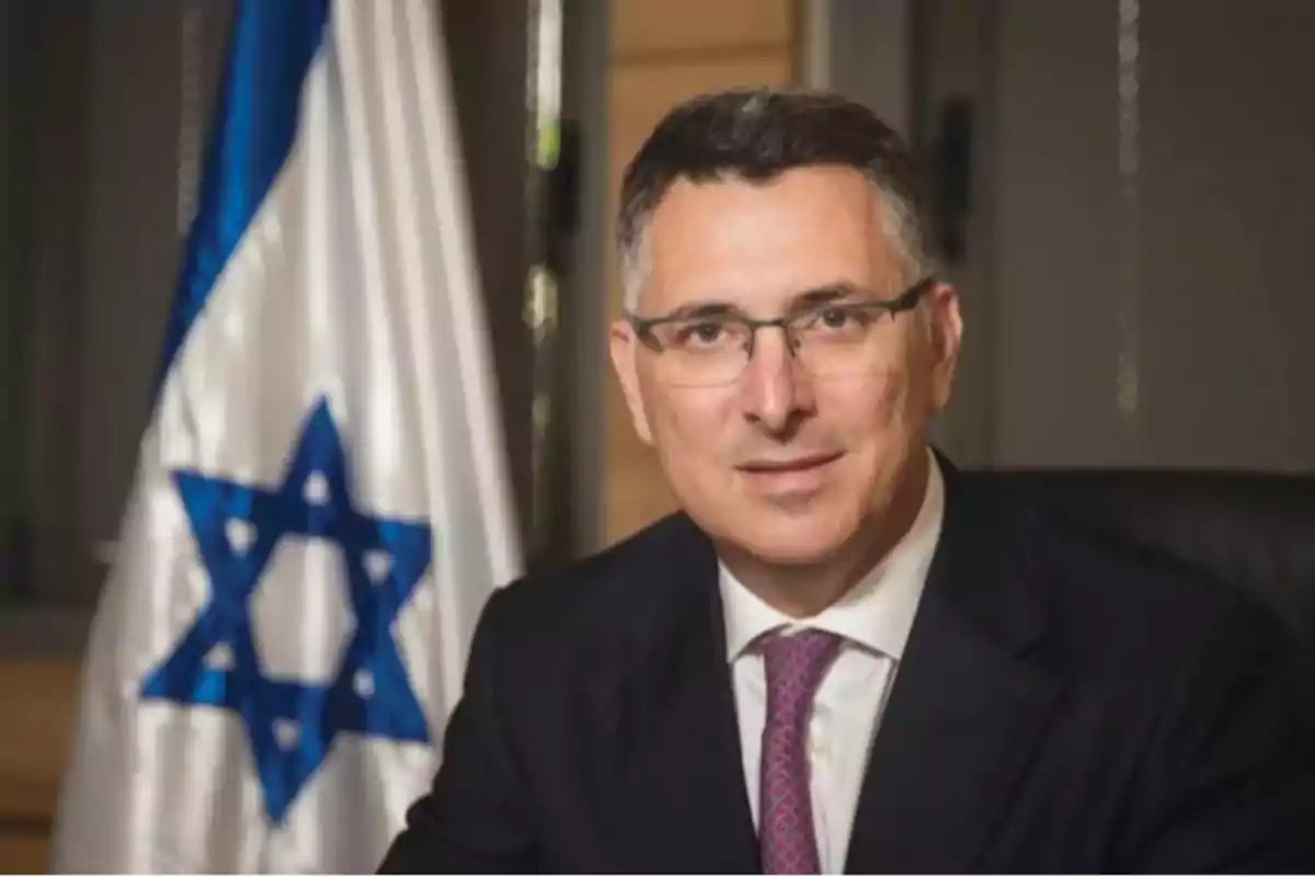 Man with glasses and a suit sitting in front of an Israeli flag Man with glasses and a suit sitting in front of an Israeli flag