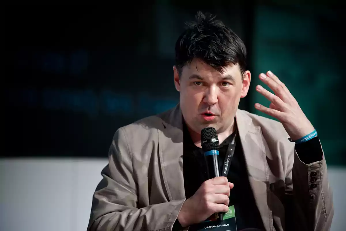Dark-haired man speaking in public while holding a microphone and gesturing with his right hand Dark-haired man speaking in public while holding a microphone and gesturing with his right hand