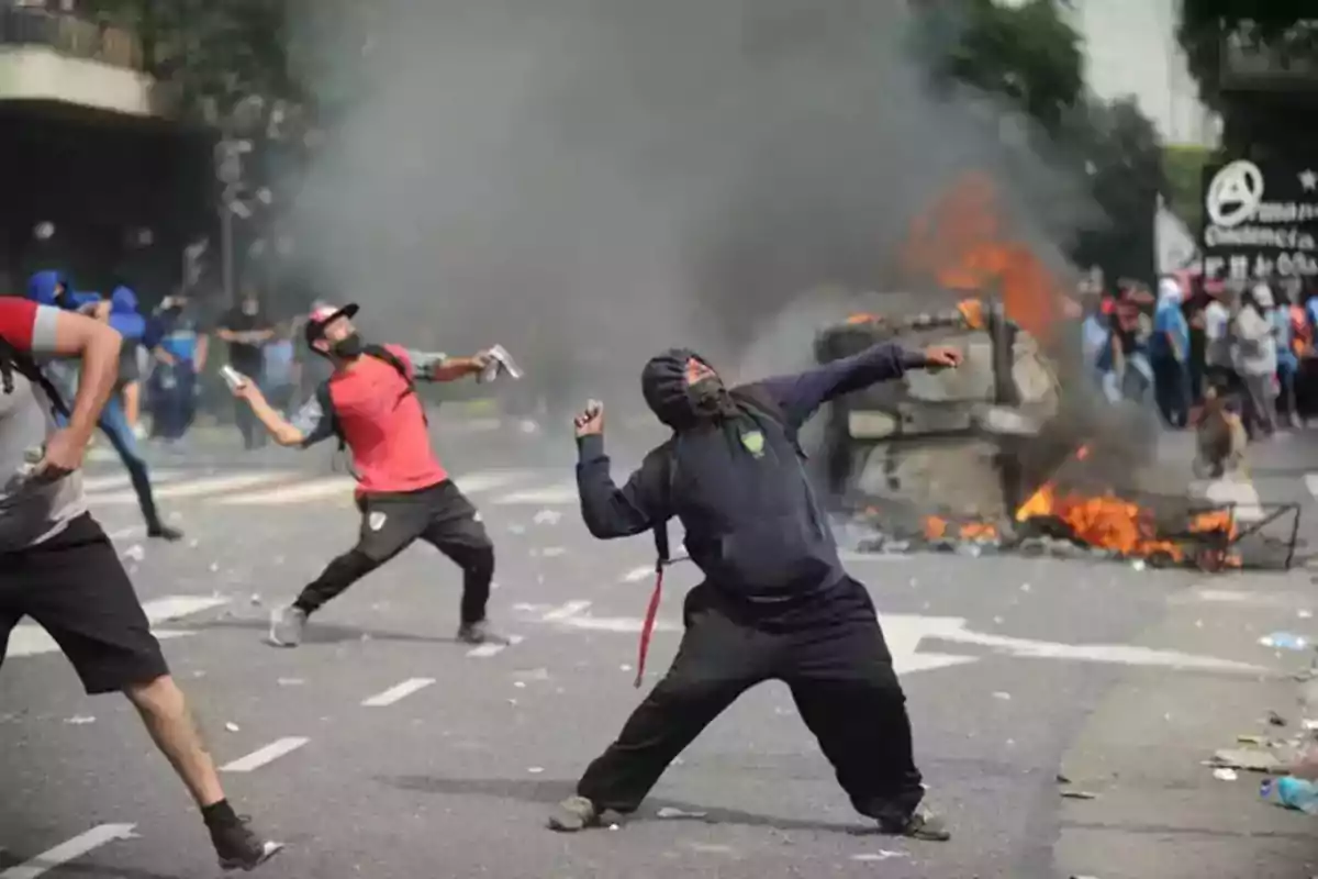 People throwing objects during a street protest with smoke and fire in the background People throwing objects during a street protest with smoke and fire in the background