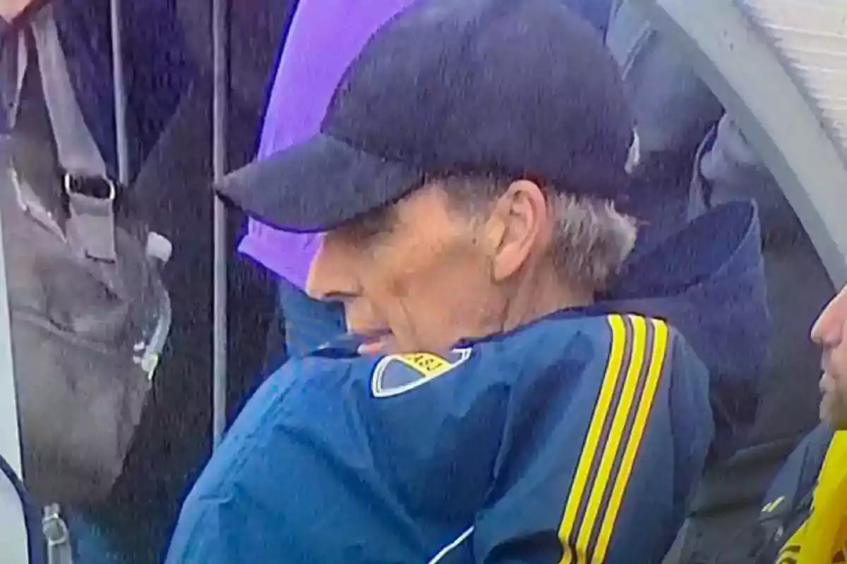 Man in profile wearing a black cap and a blue jacket with yellow stripes sitting on a bench Man in profile wearing a black cap and a blue jacket with yellow stripes sitting on a bench