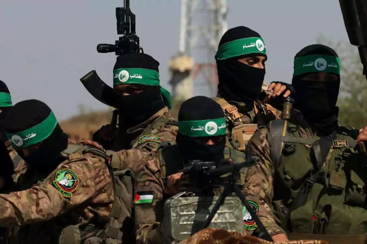 Un grupo de hombres armados con uniformes de camuflaje y pasamontañas negros con cintas verdes en la cabeza se encuentra reunido al aire libre Un grupo de hombres armados con uniformes de camuflaje y pasamontañas negros con cintas verdes en la cabeza se encuentra reunido al aire libre