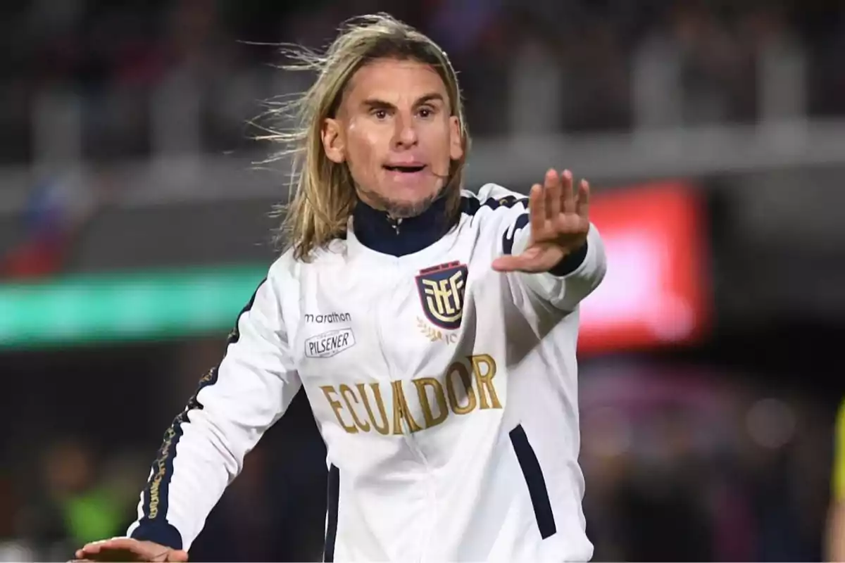 Persona con chaqueta blanca de la selección de Ecuador haciendo un gesto con la mano en un estadio. Persona con chaqueta blanca de la selección de Ecuador haciendo un gesto con la mano en un estadio.