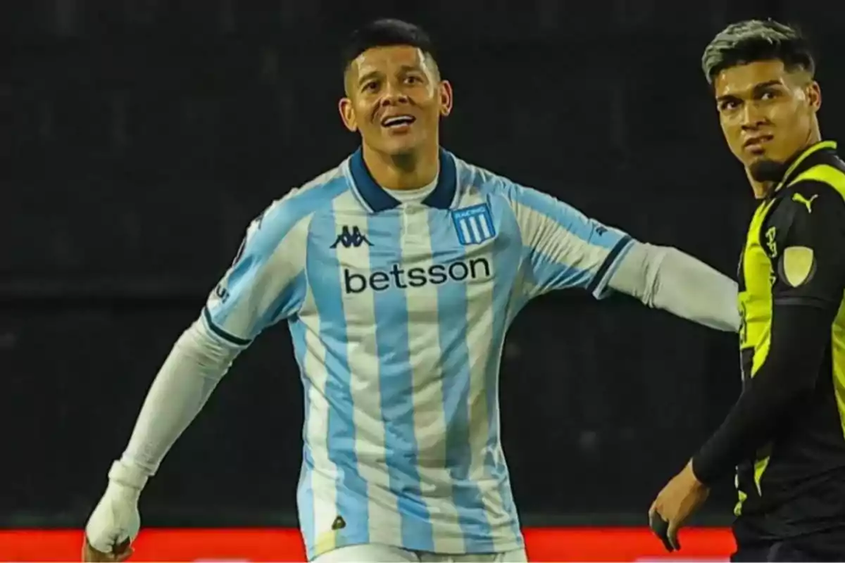 Two players in the middle of a match, one wearing Racing’s light blue and white jersey and the other wearing a black and yellow jersey. Two players in the middle of a match, one wearing Racing’s light blue and white jersey and the other wearing a black and yellow jersey.