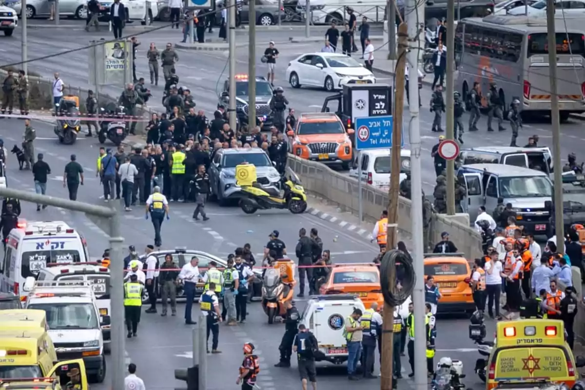 Numerous emergency vehicles and police personnel are gathered on a blocked avenue while several people watch the scene and some officers direct traffic and manage the situation. Numerous emergency vehicles and police personnel are gathered on a blocked avenue while several people watch the scene and some officers direct traffic and manage the situation.