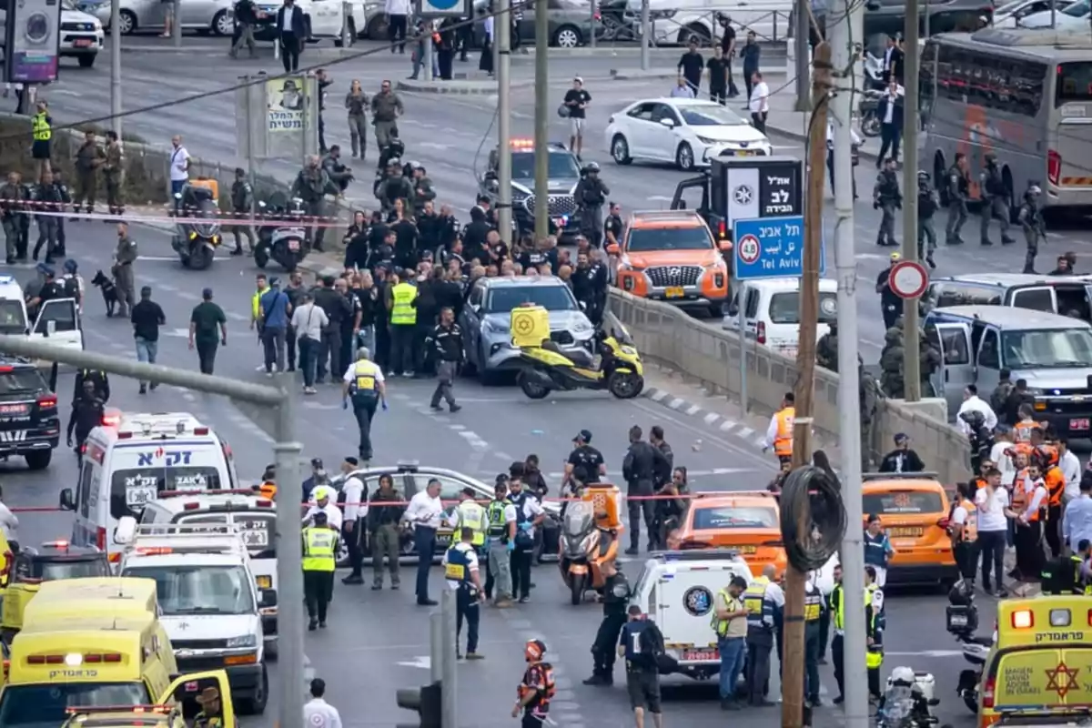 A large number of police officers, paramedics, and emergency vehicles are on a cordoned-off avenue, surrounded by cars and people, in what appears to be an emergency situation in a city.