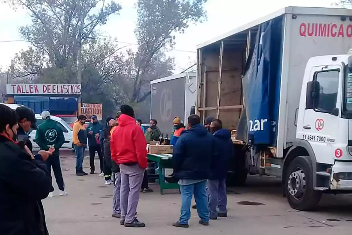 Un grupo de personas reunidas junto a un camión de carga en un taller de elásticos al aire libre Un grupo de personas reunidas junto a un camión de carga en un taller de elásticos al aire libre