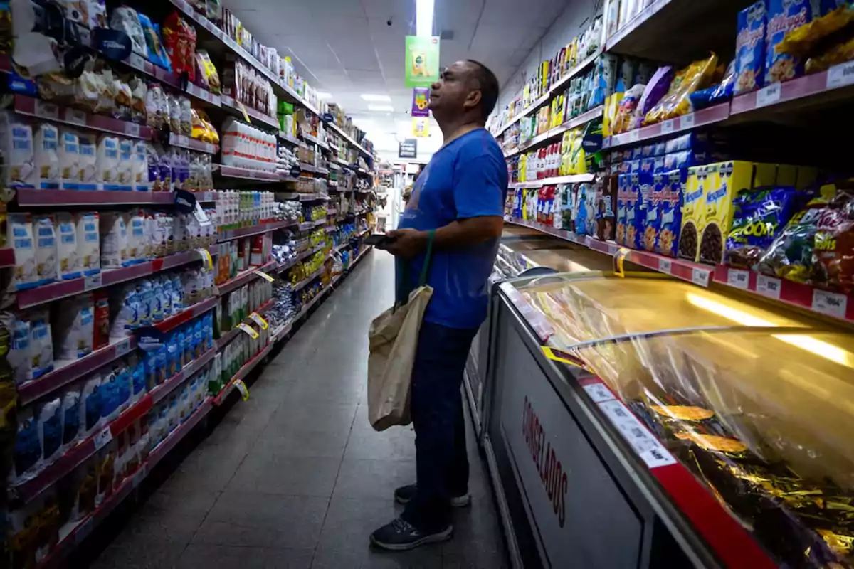 Man wearing a blue t-jersey and carrying a tote bag shopping in a supermarket aisle surrounded by shelves full of products Man wearing a blue t-jersey and carrying a tote bag shopping in a supermarket aisle surrounded by shelves full of products