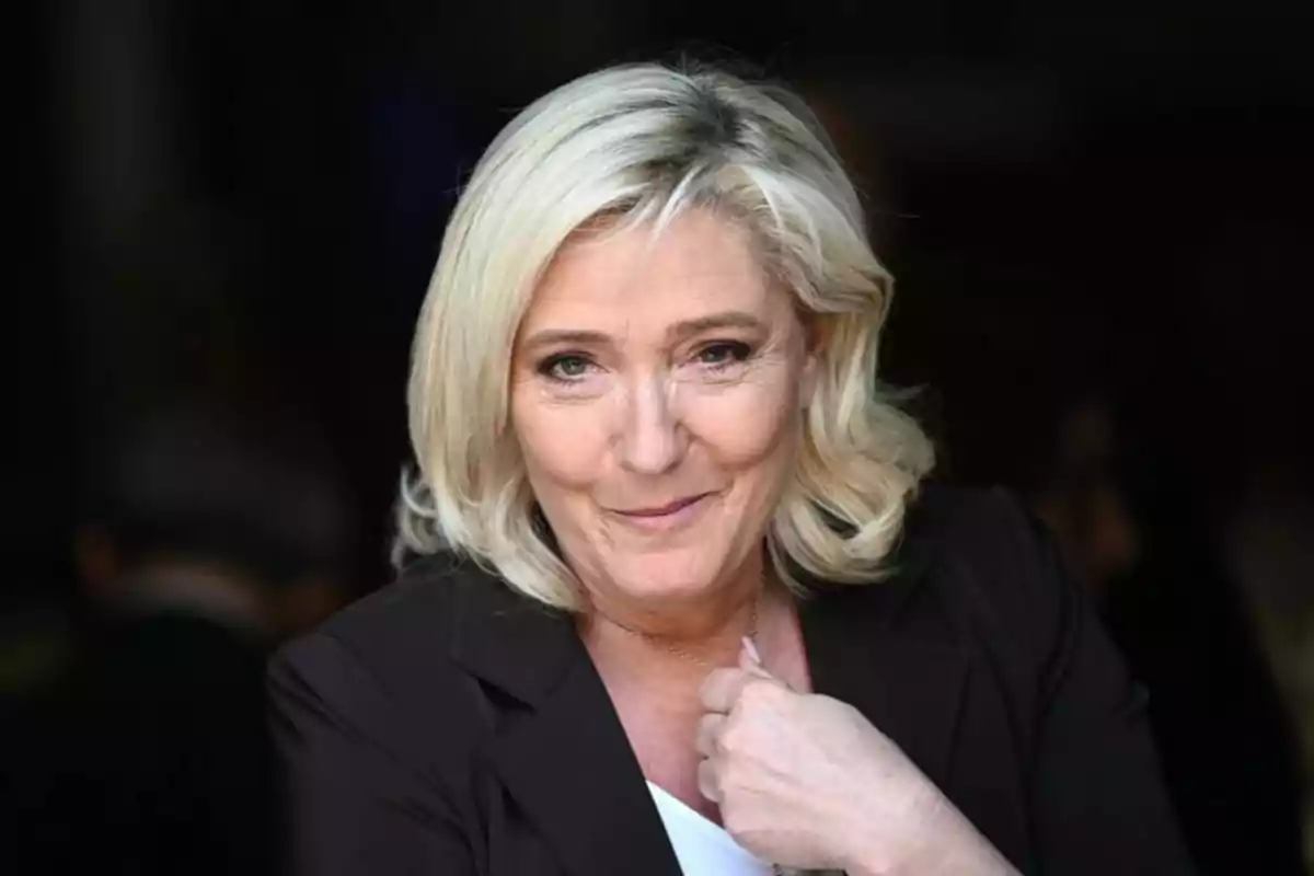 Blonde woman with short, wavy hair wearing a dark jacket, looking at the camera and smiling slightly Blonde woman with short, wavy hair wearing a dark jacket, looking at the camera and smiling slightly