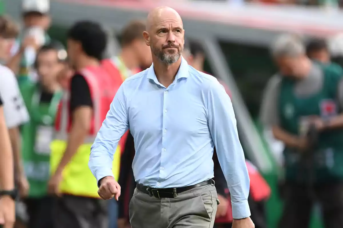 Bald man with a beard and a blue jersey walking in a soccer stadium with blurred people in the background