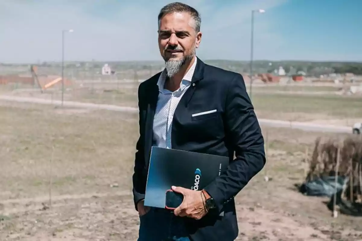 Gray-bearded man in a dark suit and light jersey holding a folder and a phone on an outdoor site Gray-bearded man in a dark suit and light jersey holding a folder and a phone on an outdoor site