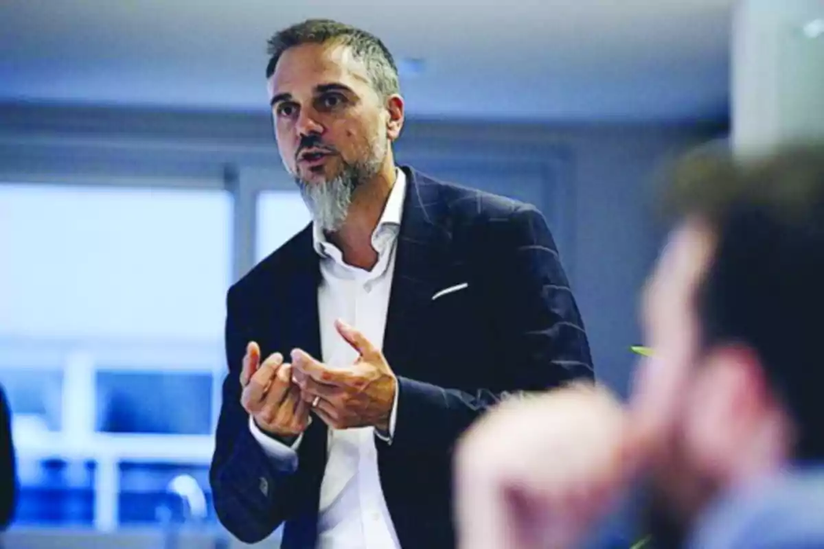 Gray-bearded man in a dark jacket speaking and gesturing during a meeting in an office. Gray-bearded man in a dark jacket speaking and gesturing during a meeting in an office.