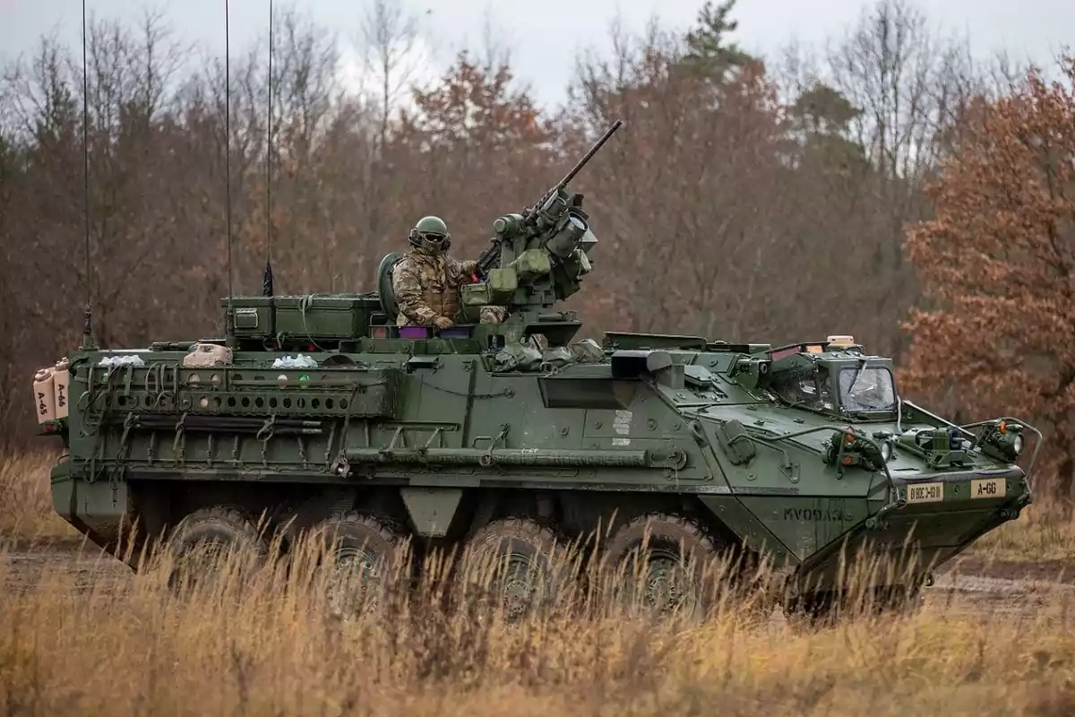Six-wheeled armored military vehicle with a soldier on board in a wooded environment during autumn