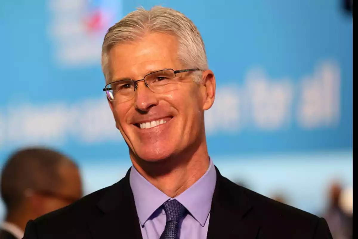 Hombre de cabello canoso y gafas sonriendo con fondo azul desenfocado Hombre de cabello canoso y gafas sonriendo con fondo azul desenfocado