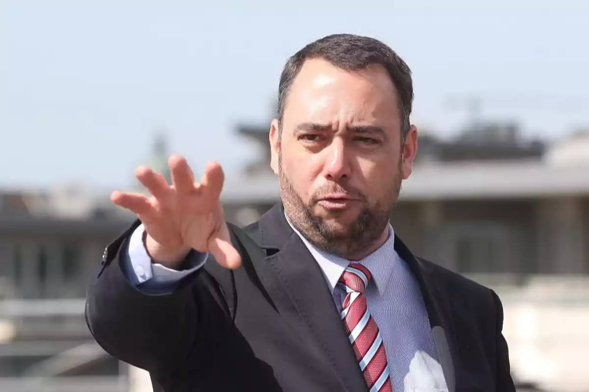Hombre de traje y corbata haciendo un gesto con la mano extendida al frente en un entorno urbano al aire libre Hombre de traje y corbata haciendo un gesto con la mano extendida al frente en un entorno urbano al aire libre
