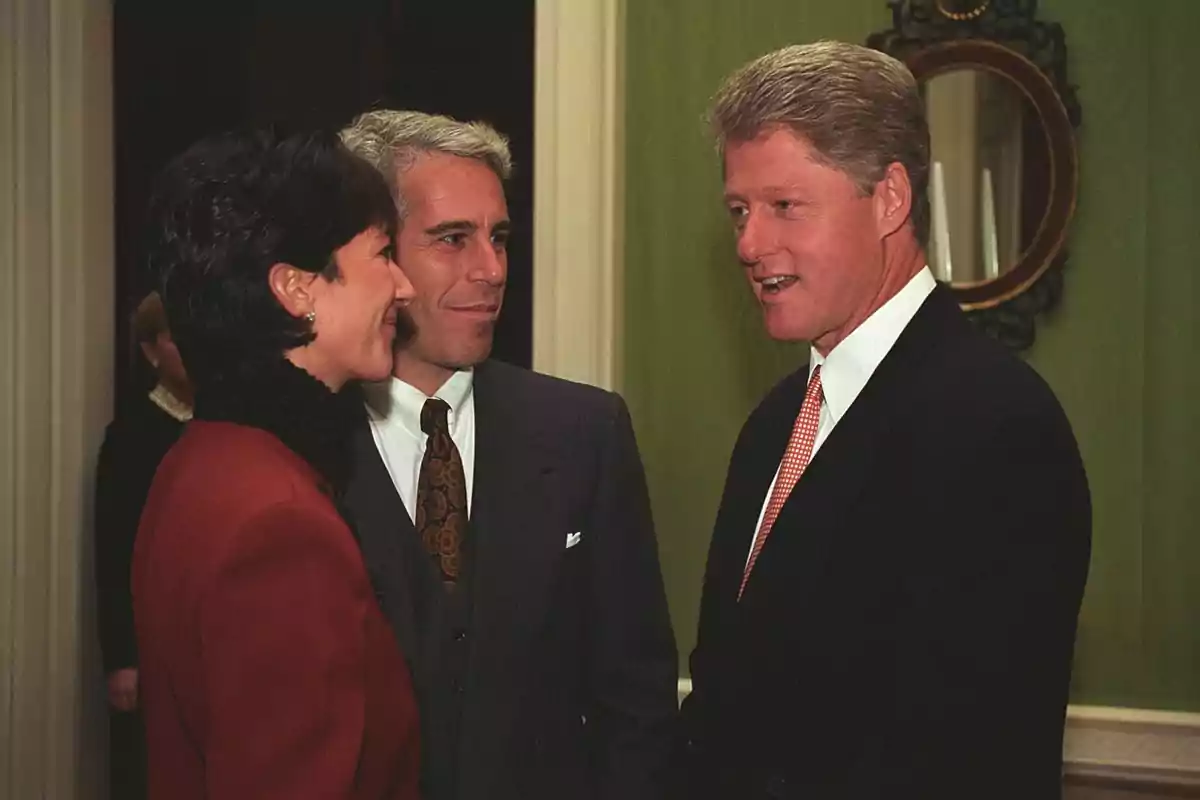 Three elegantly dressed people are conversing in a room with green walls and a decorative mirror in the background. Three elegantly dressed people are conversing in a room with green walls and a decorative mirror in the background.