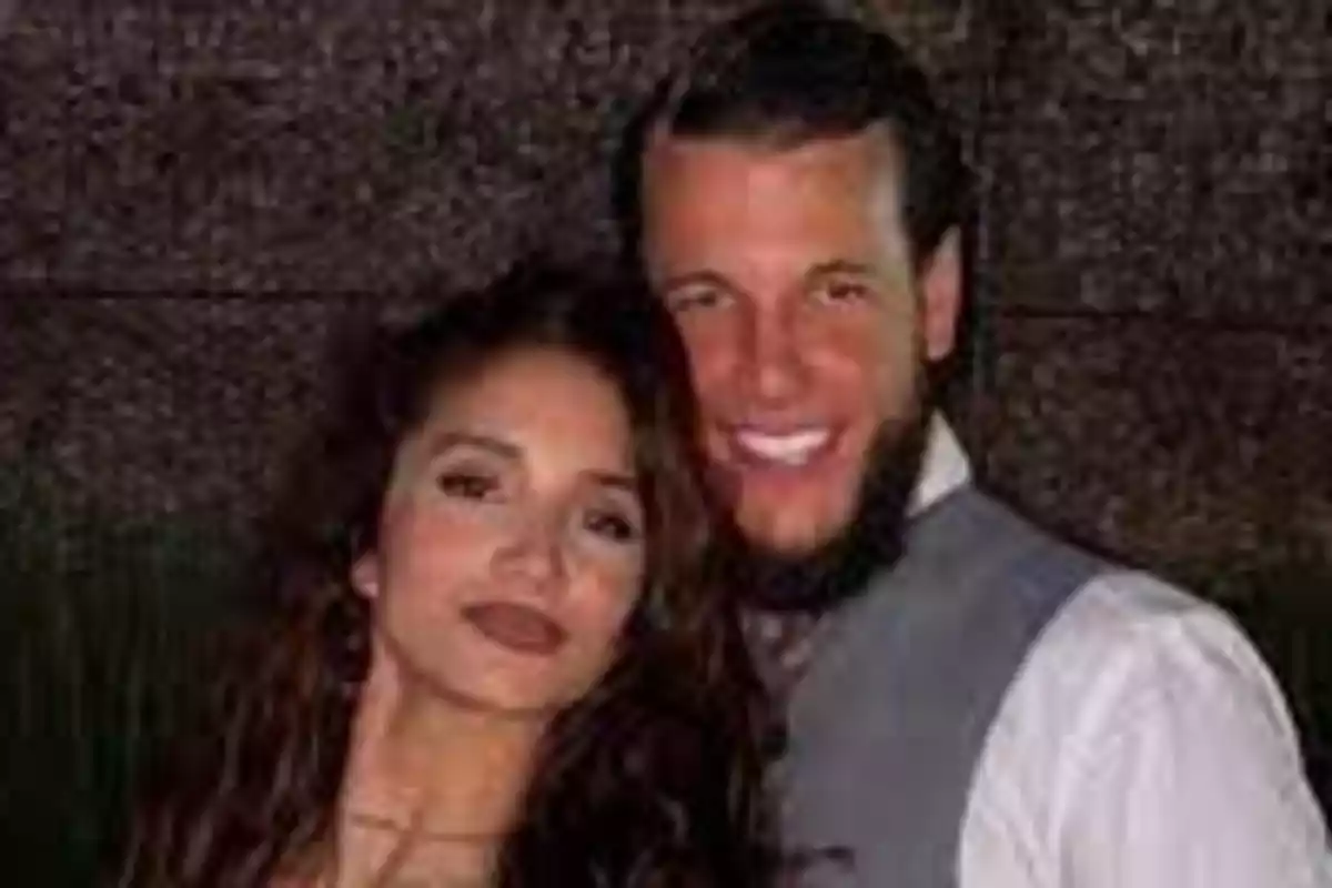 A young couple poses hugging and smiling in front of a dark wall.