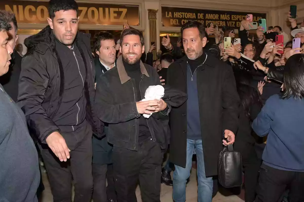 A smiling man walks surrounded by security while a crowd of people takes photos of him with their cell phones. A smiling man walks surrounded by security while a crowd of people takes photos of him with their cell phones.