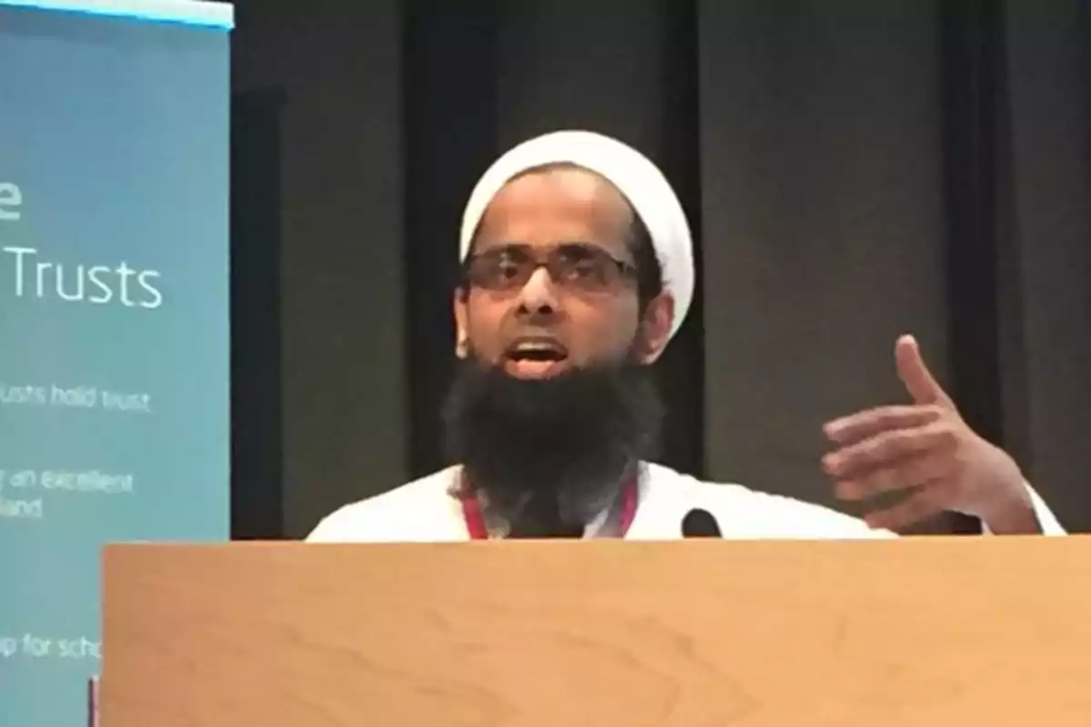 Hombre con barba y turbante blanco hablando en un podio durante una presentación Hombre con barba y turbante blanco hablando en un podio durante una presentación