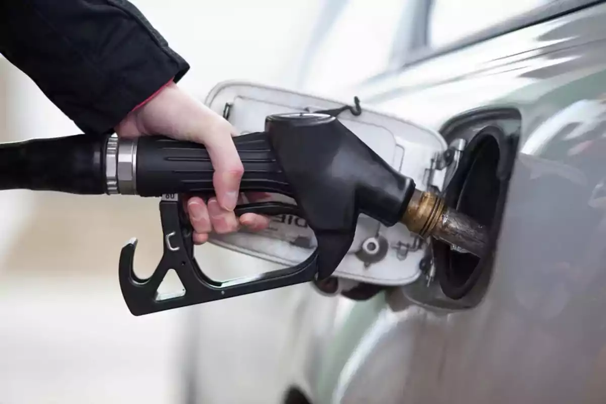 Persona sosteniendo una manguera de gasolina mientras carga combustible en un automóvil plateado Persona sosteniendo una manguera de gasolina mientras carga combustible en un automóvil plateado