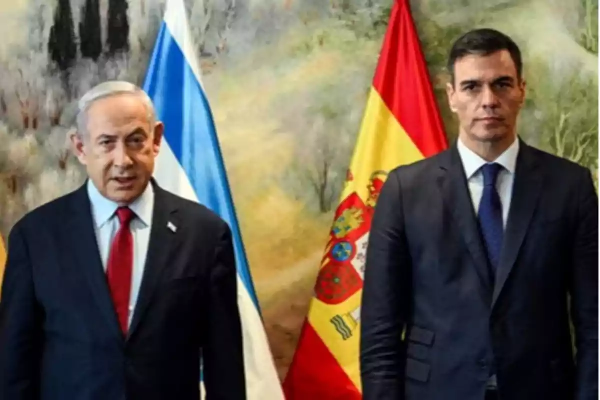 Two men in suits pose in front of the flags of Israel and Spain in a formal setting.