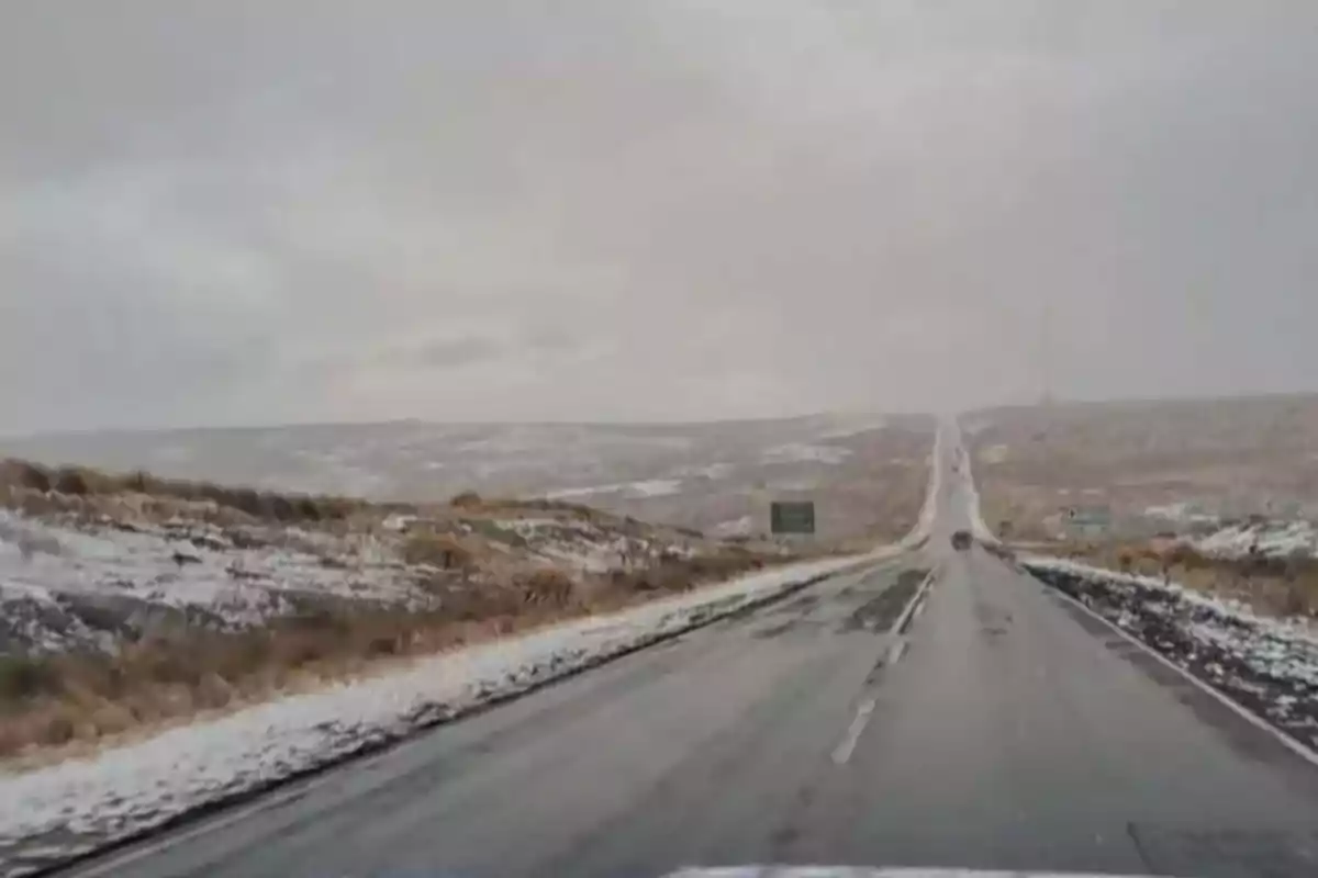 Straight road in the middle of a rural landscape with light snow covering the ground and a cloudy sky Straight road in the middle of a rural landscape with light snow covering the ground and a cloudy sky